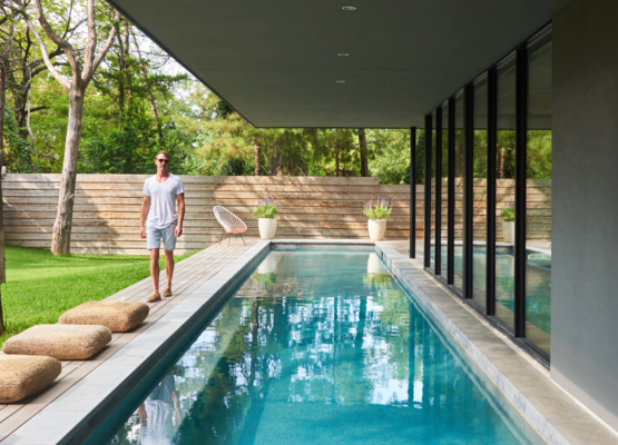 SliderEvolution-01 Modern backyard pool beside glass-walled house with man standing on deck.